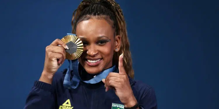 Rebeca Andrade, ginasta brasileira, segura sua medalha e faz o sinal de '1' com a outra mão