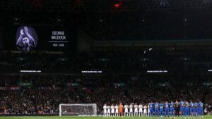 Jogadores de Inglaterra e Grécia se reúnem no meio do campo para prestar um minuto de silêncio, em homenagem a George Baldock