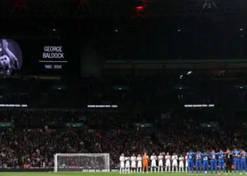Jogadores de Inglaterra e Grécia se reúnem no meio do campo para prestar um minuto de silêncio, em homenagem a George Baldock
